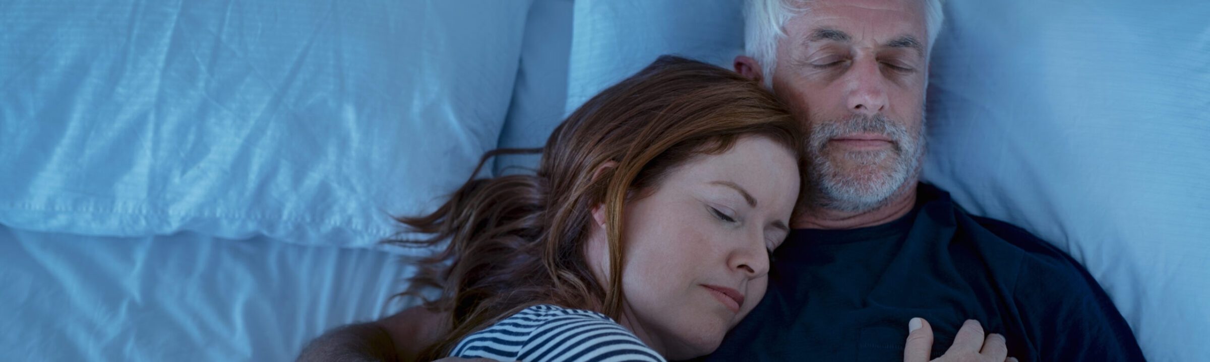 A happy middle-aged couple is sleeping in bed peacefully after getting the Snore Treatment in Victoria