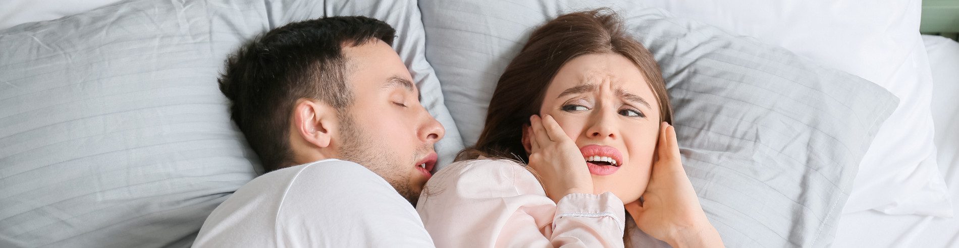 A person is awakened to their partner's loud snoring as they cover their ears. Victoria Snore Treatment.